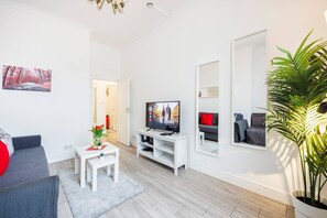 Un salon moderne avec un téléviseur, un canapé, une table basse et une plante en pot.