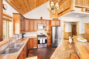 Eine Küche mit Holzausstattung, Edelstahlgeräten, Granit Arbeitsplatten und einer Pendelleuchte.
