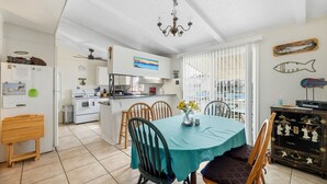 A compact kitchen with a dining area, featuring a teal table, wooden chairs, and a view through large windows. - Estes Flat -Private Dock-Fish cleaning station, Fish Camp (Rockport)