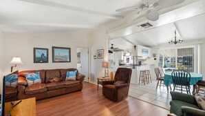 A spacious living room with a brown leather sofa, a wooden coffee table, and a dining area with a green tablecloth. - Estes Flat -Private Dock-Fish cleaning station, Fish Camp (Rockport)