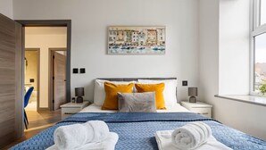 Un hotel moderno con una cama grande, dos mesitas de noche, un cuadro en la pared y vistas al exterior.