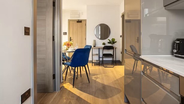 Una cocina moderna con refrigerador empotrado, un comedor con sillas azules y piso de madera.