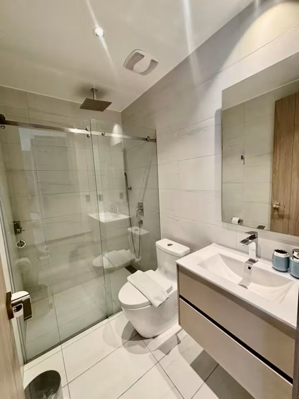 Een moderne badkamer met een douche met glazen wand, een wit toilet en een wastafel met spiegel.