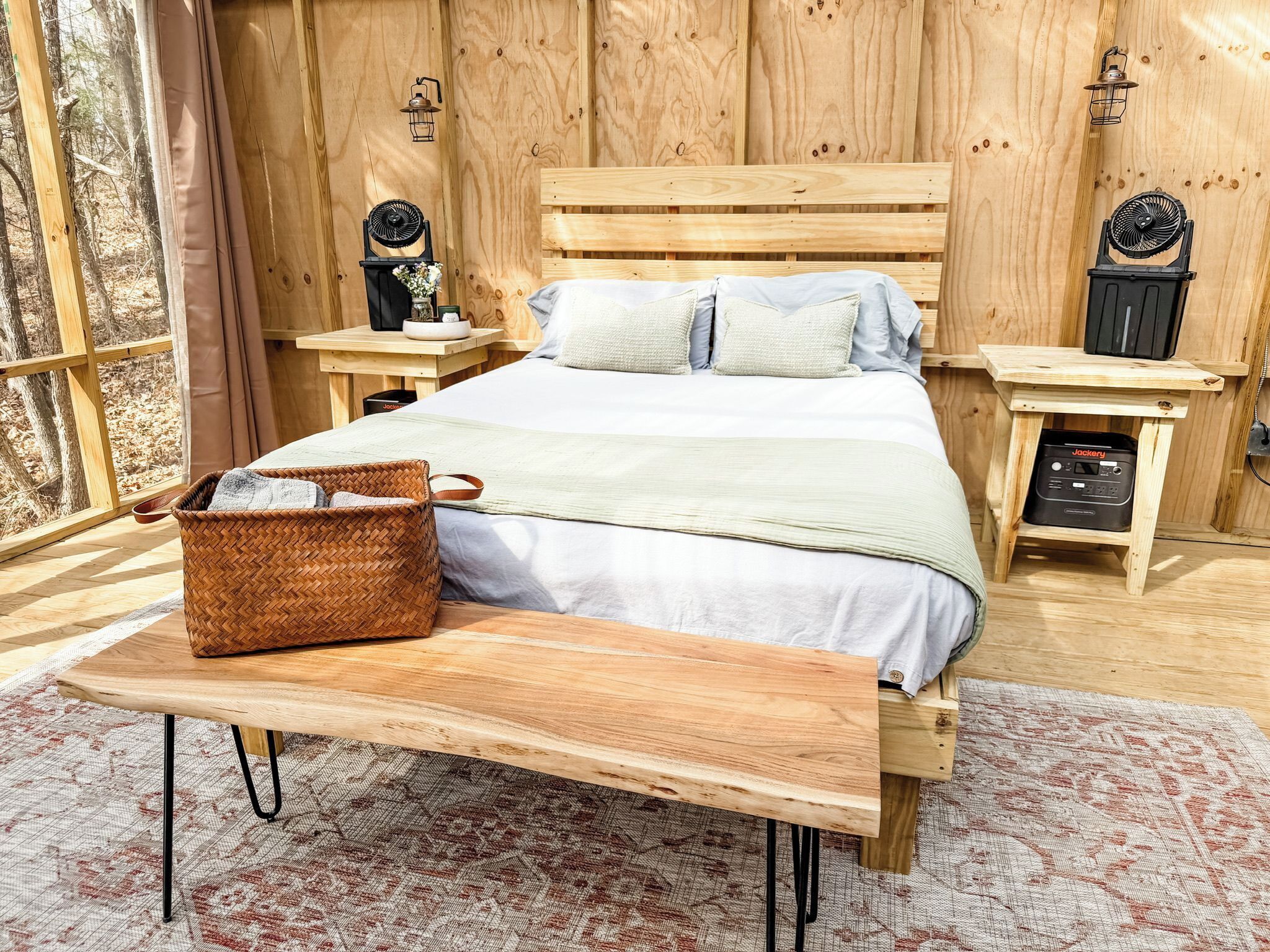 Un dormitorio de cabaña de madera con una cama, mesitas de noche, una cesta tejida y un banco.