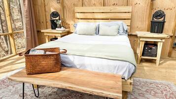 Un dormitorio de cabaña de madera con una cama, mesitas de noche, una cesta tejida y un banco.