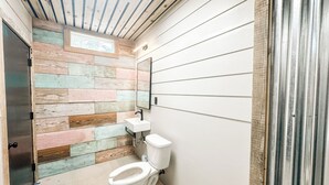 Une salle de bain avec un mur recouvert de planches de bois, un lavabo blanc et des toilettes.