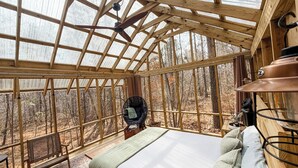 Une pièce confortable avec un lit, une chaise et une table, agrémentée d’une grande fenêtre et de poutres en bois.
