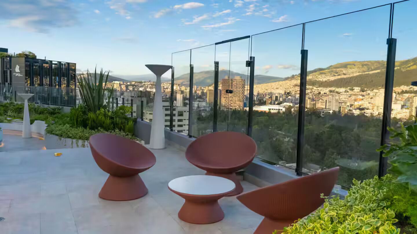 A rooftop terrace with modern furniture, glass walls, and a city view.