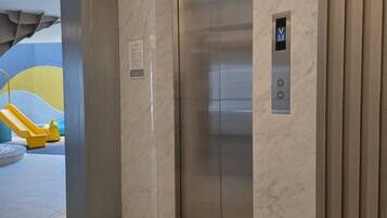 Un ascenseur moderne doté d’un panneau de commande, de murs en marbre et d’un espace de jeux avec des équipements jaunes.