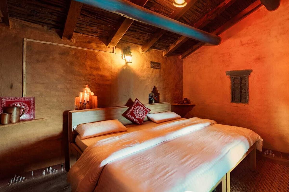 Ein traditionell eingerichtetes Zimmer mit einem hölzernen Bett, einem Nachttisch mit Kerzen und einer rustikalen Wand.
