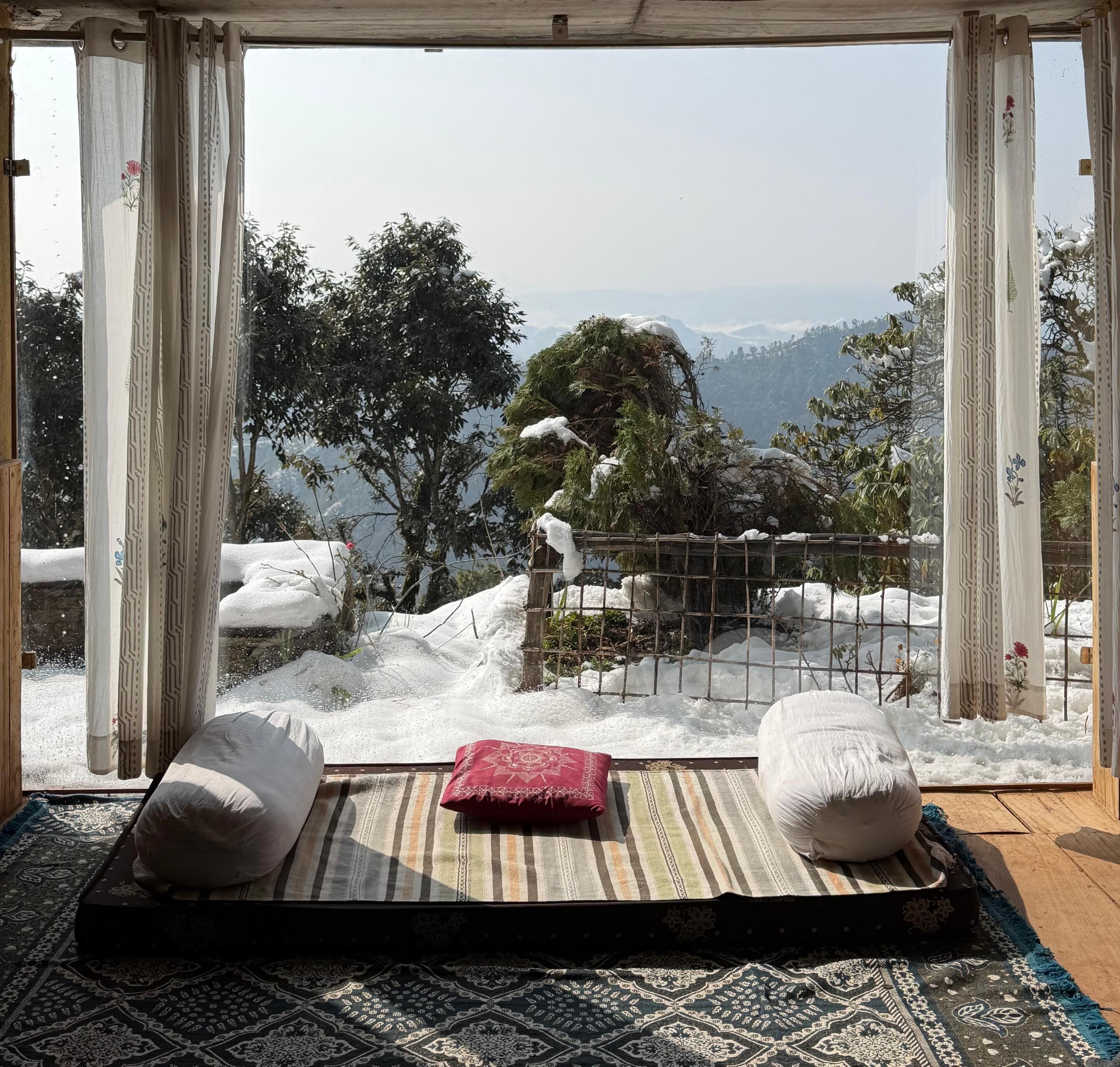 Una habitación con vistas a montañas nevadas, suelo de madera y un felpudo con almohadones.