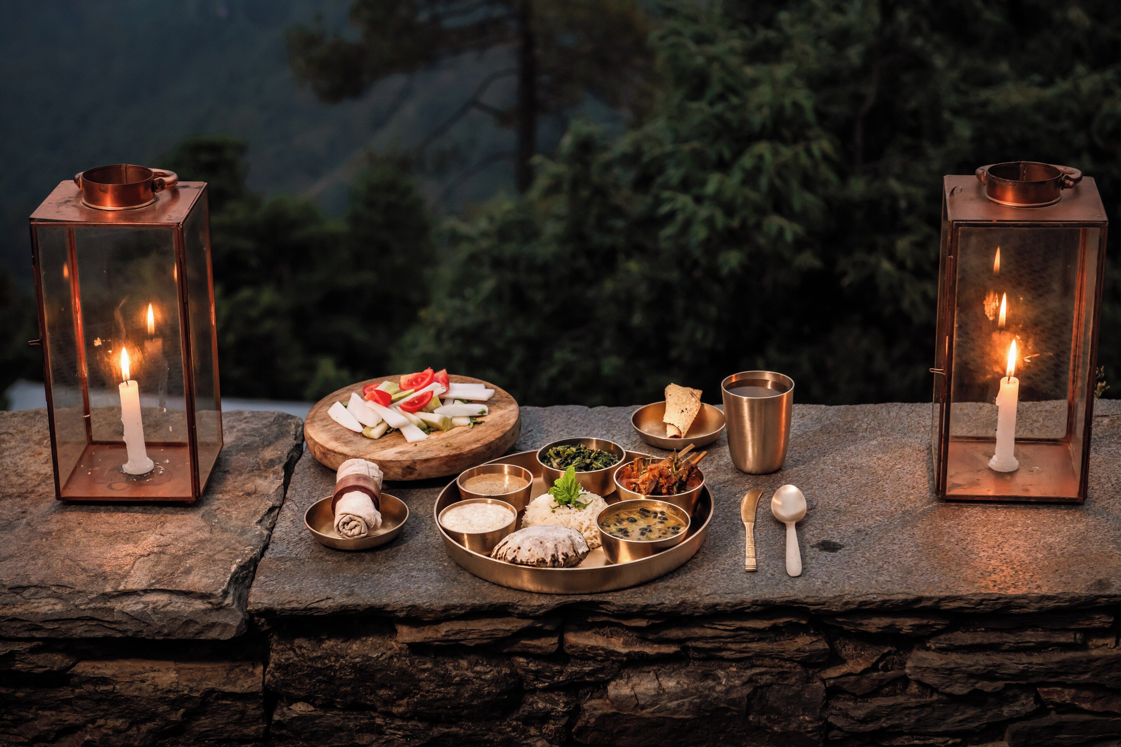 A stone table with a meal and two lanterns, set against a forest backdrop.