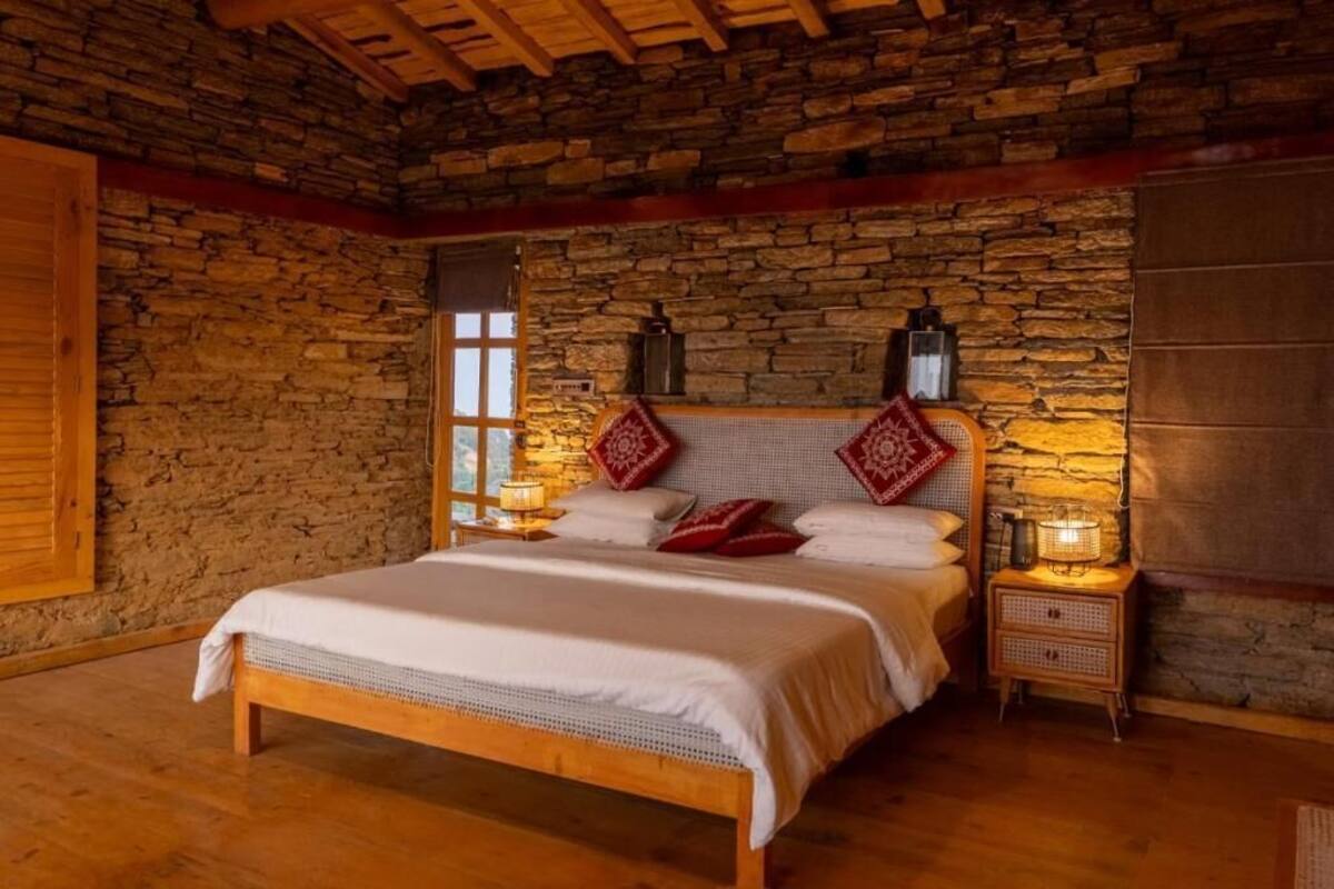 Ein rustikales Schlafzimmer mit Steinwand, hölzernem Bettgestell und zwei Nachttischen mit Lampen.