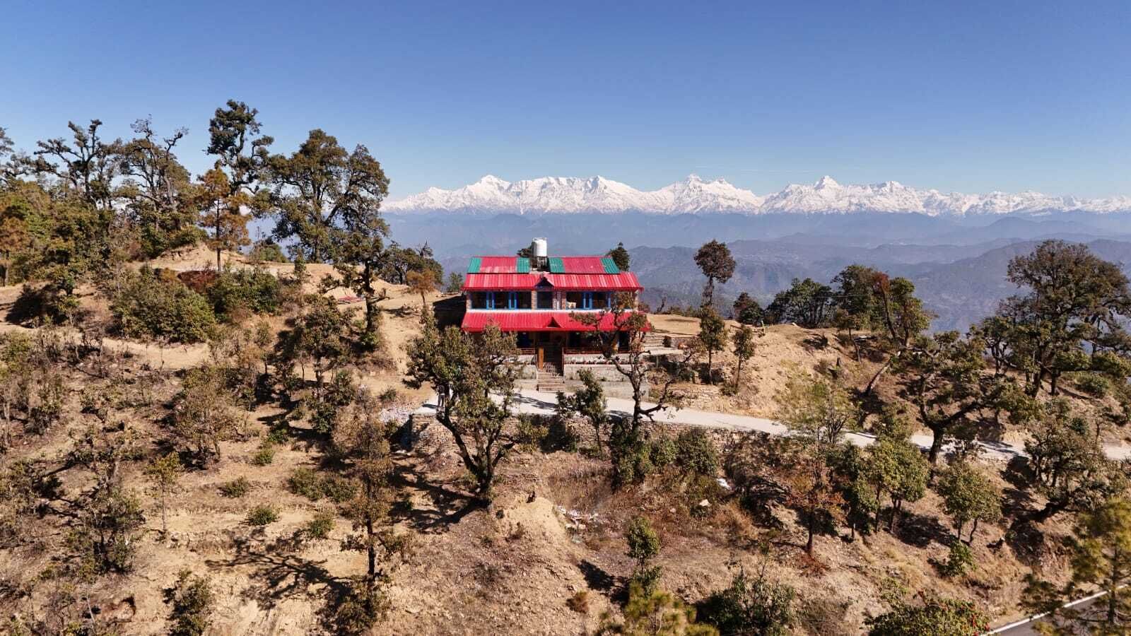A red-roofed building with a staircase leading up to it, surrounded by sparse vegetation and snow-capped mountains in the background.