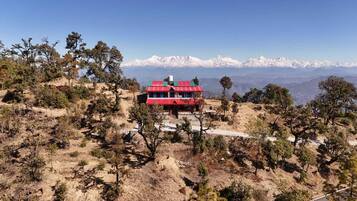 A red-roofed building with a staircase leading up to it, surrounded by sparse vegetation and snow-capped mountains in the background.