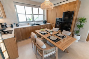 Une cuisine moderne avec des meubles en bois, un grand îlot central doté de sièges, un réfrigérateur noir et un luminaire suspendu.