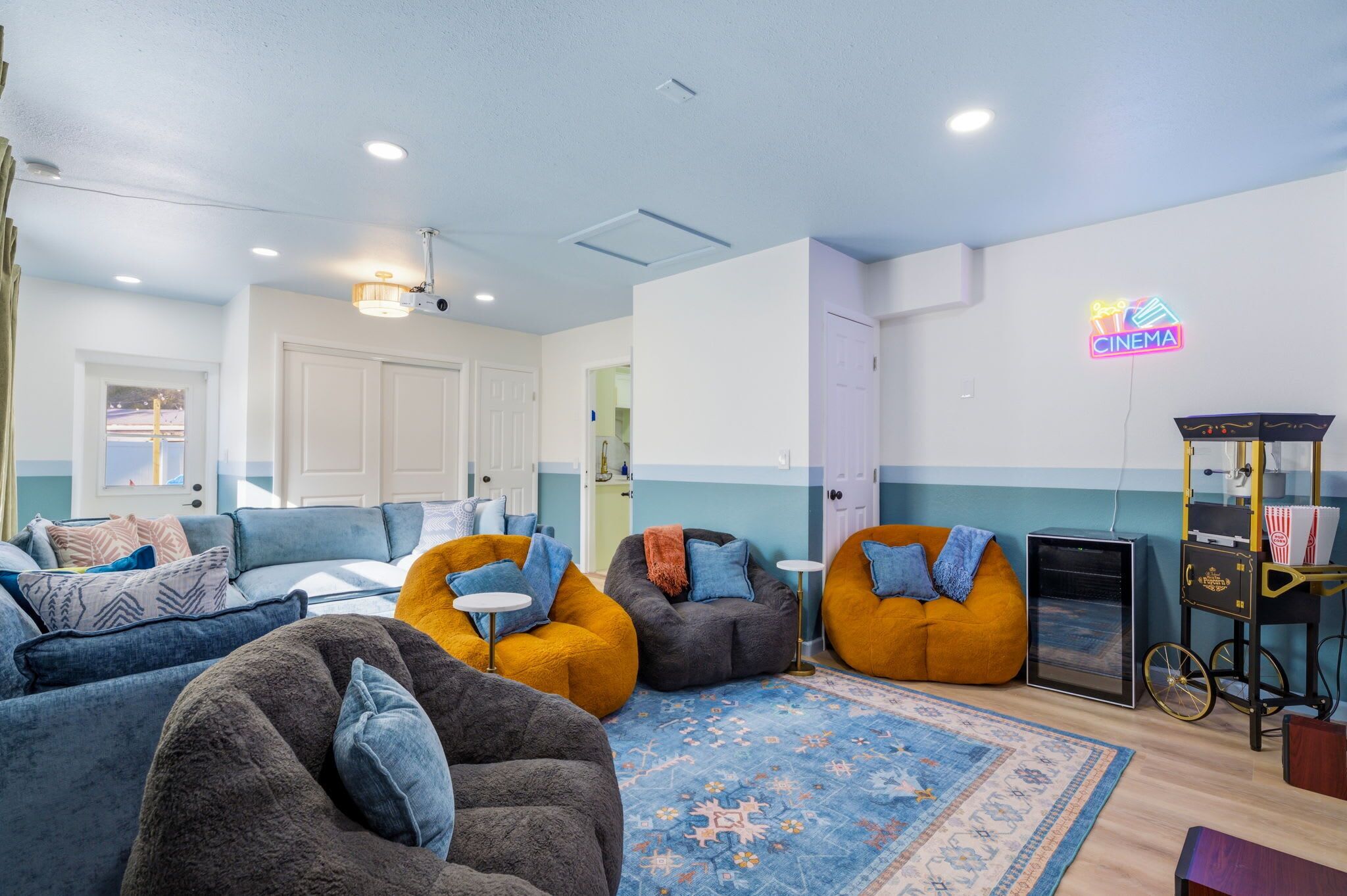 A cozy living area with blue and orange seating, a cinema sign, and a vintage projector cart.