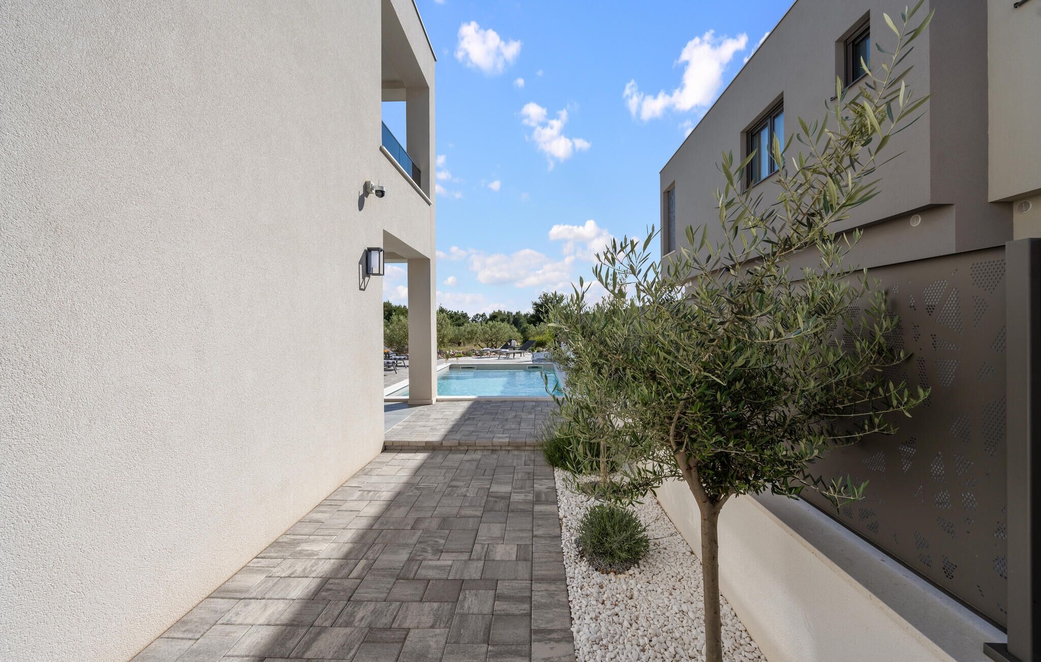 A pool area with a clear sky, a paved walkway, and a small tree.