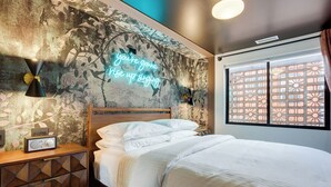 Un dormitorio con cama, pared con estampado floral, letrero de neón y ventana con celosía decorada.