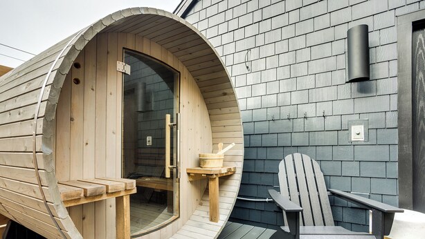 Una sauna de madera con una entrada curva, un banco de madera y una silla de sauna en una terraza.