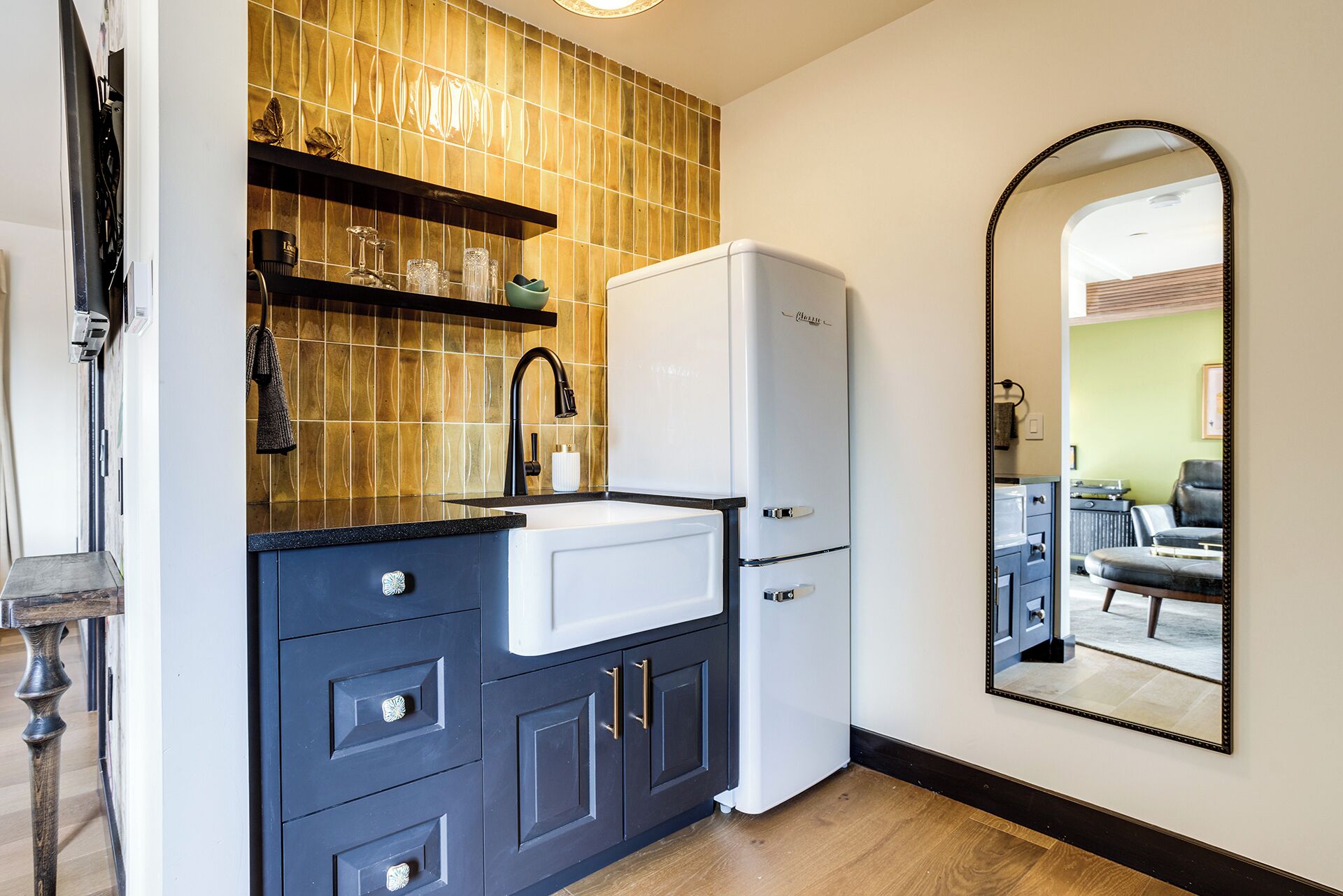 A kitchen with a white refrigerator, dark blue cabinets, a black countertop, and a tiled backsplash.