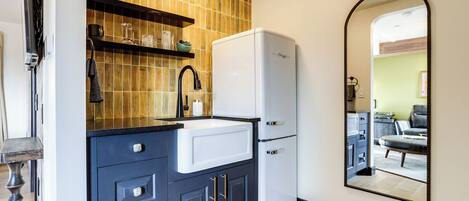 A kitchen with a white refrigerator, dark blue cabinets, a black countertop, and a tiled backsplash.