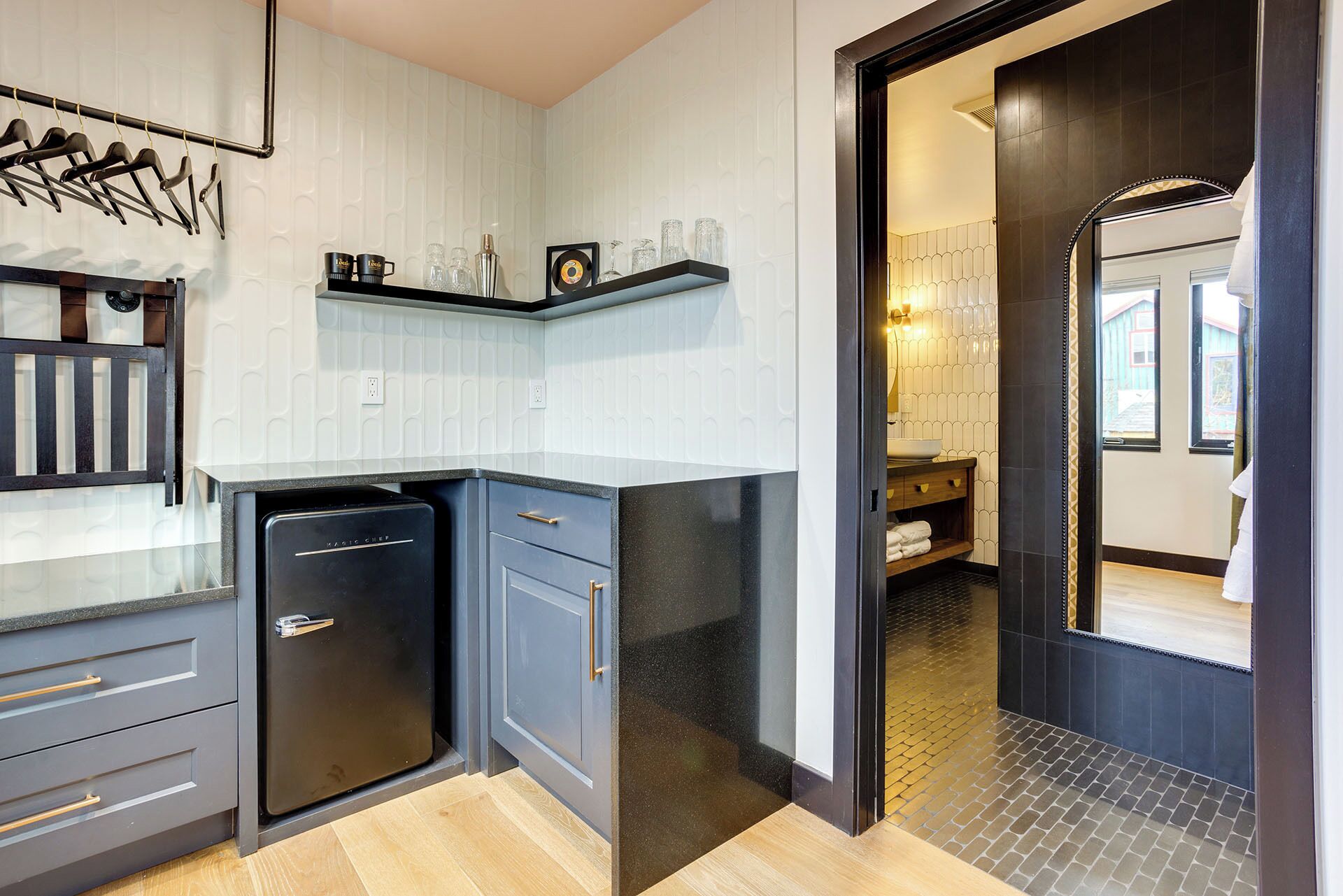 A modern kitchen with grey cabinets, a black refrigerator, and a hanging rack.