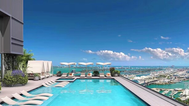 Piscina infinita en la azotea con sillones de descanso y sombrillas, con vistas a un paisaje urbano y la costa.