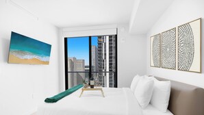 Un hotel moderno con una cama grande, vistas de la ciudad a través de ventanas de piso a techo, un cuadro de una playa y decoración artística en la pared.