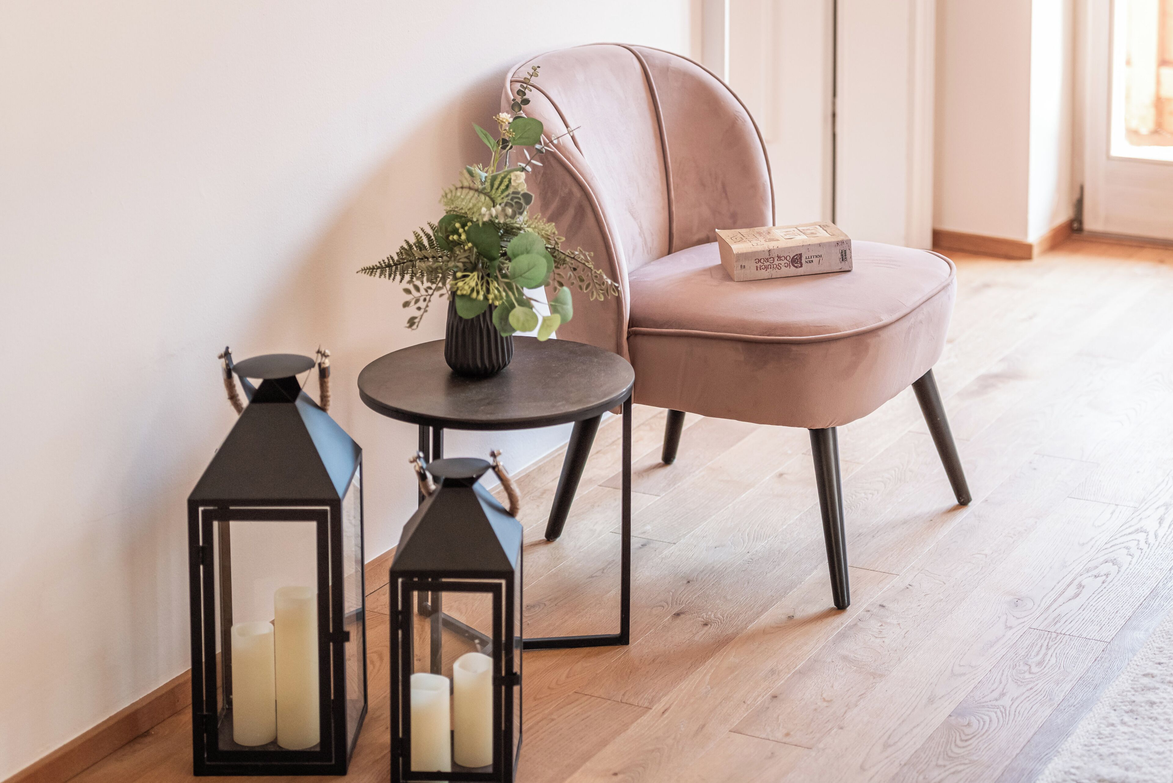 Ein Zimmer mit Sesseln, einem runden Tisch und zwei schwarzen Laternen mit Kerzen.