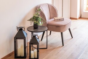Ein Zimmer mit Sesseln, einem runden Tisch und zwei schwarzen Laternen mit Kerzen.