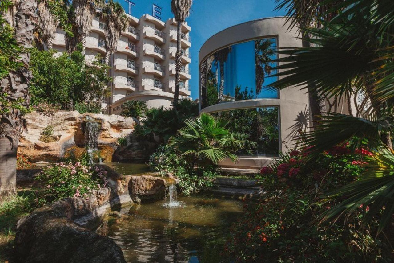 Un hôtel doté d’un espace piscine agrémenté d’une cascade, le tout entouré d’une végétation luxuriante et de palmiers.