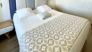 Ein modernes Hotelzimmer mit einem großen Bett, einem Nachttisch und einem wandmontierten Spiegel.