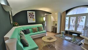 Ein modernes Wohnzimmer mit einem grünen Sofa, einem runden Couchtisch und Blick ins Freie durch ein großes Fenster.