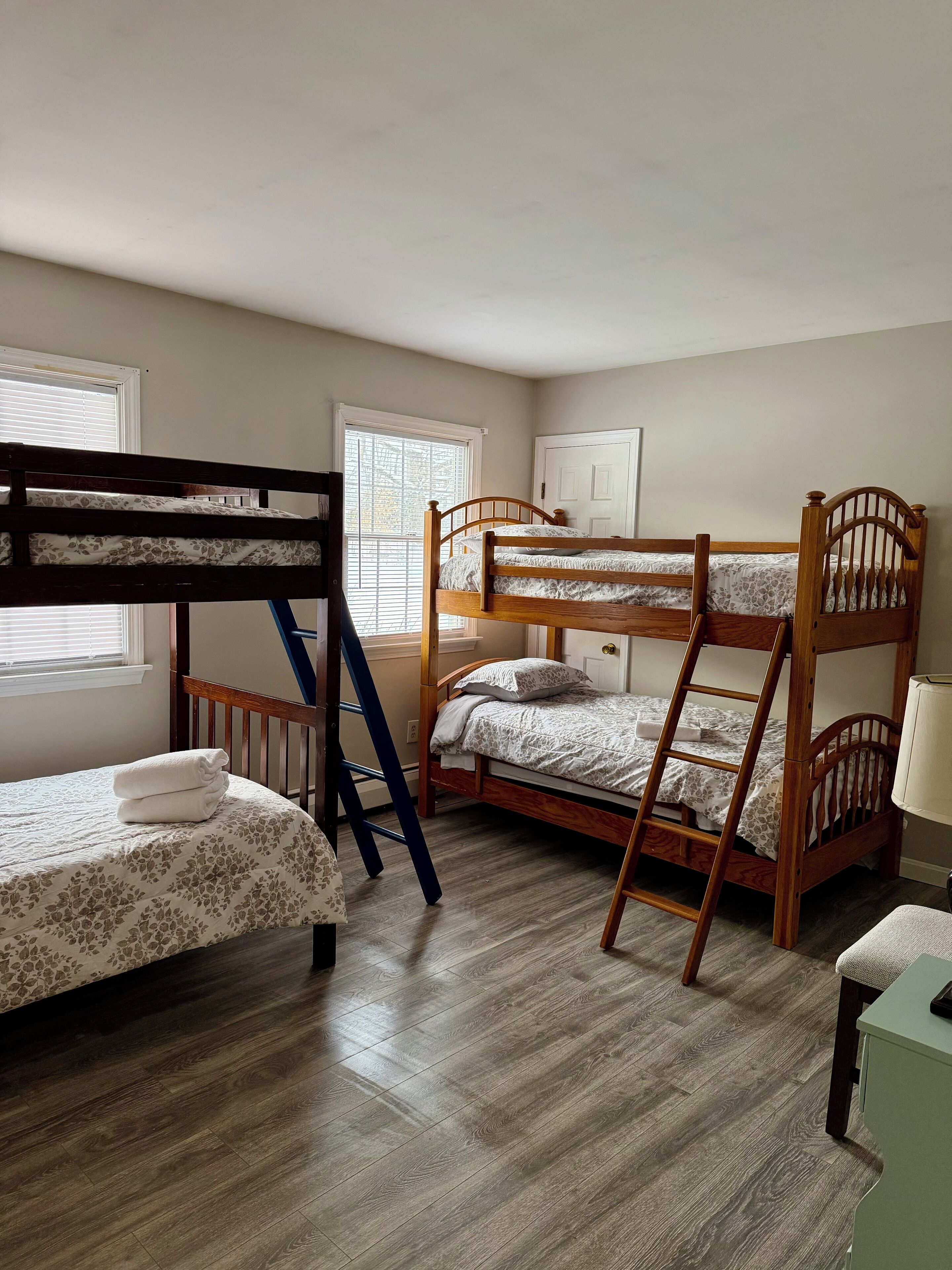 A room with two bunk beds, a wooden ladder, and a small table with a lamp.