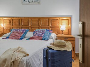 A neatly made bed with patterned pillows, a bedside lamp, and a suitcase with a hat on top.