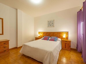 A bedroom with a large bed, wooden headboard, two bedside tables with lamps, a wooden dresser, and a purple curtain.