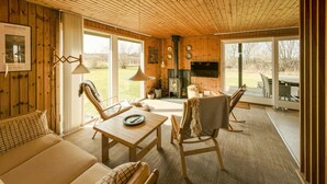 Ein gemütliches Blockhaus-Interieur mit Holzwänden, Kamin, Essbereich und Blick ins Freie.