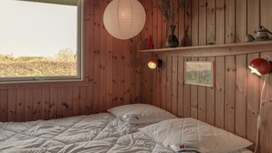 Ein Zimmer mit Holzboden, einem Bett, einem Fenster, einer Wandlampe und einem Regal mit Dekorationen.