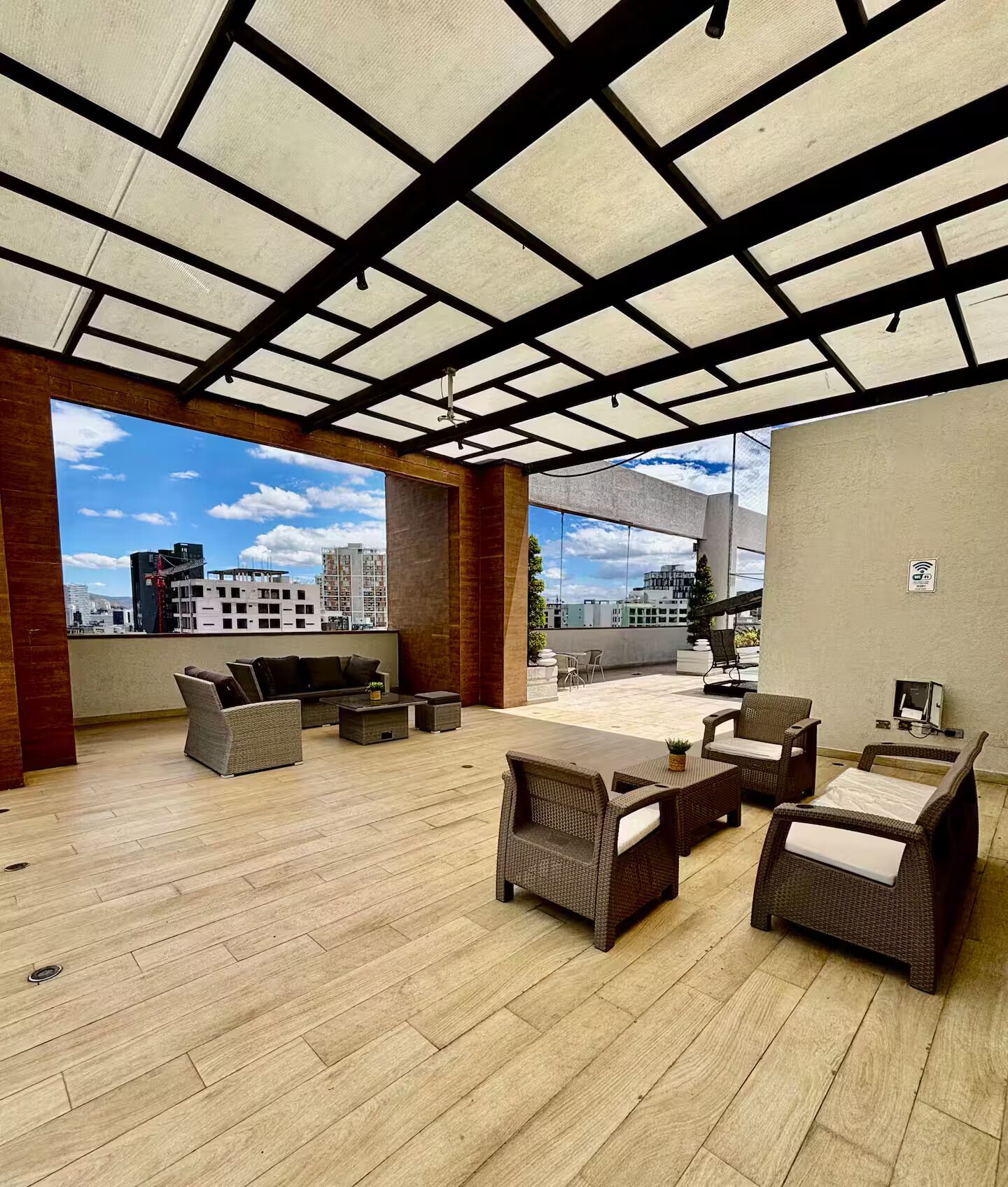 An outdoor patio area with wicker furniture, a ceiling with a grid pattern, and a view of buildings in the background.