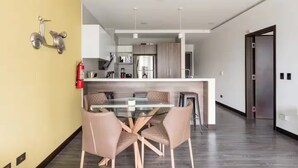 Una cocina moderna con electrodomésticos de acero inoxidable, una mesa de vidrio con cuatro sillas y un extintor en la pared.
