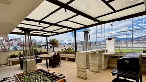Un espacio interior amplio con una mesa de fútbol de mesa, asientos exteriores y vistas de la ciudad a través de grandes ventanales.