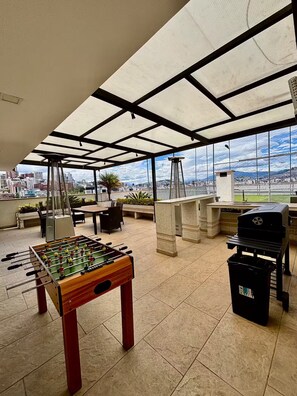 Ein geräumiger Innenbereich mit einem Tischfußballtisch, Sitzgelegenheiten im Freien und Blick auf die Stadt durch große Fenster.