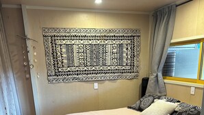 A bedroom with a bed, a patterned tapestry, curtains, and a window.