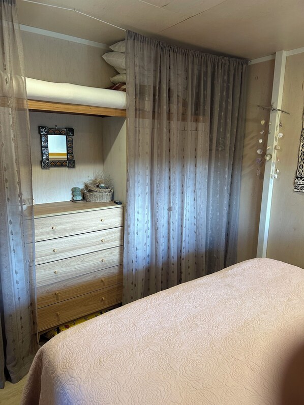 Un dormitorio con una cama litera, un aparador de madera, un espejo y una cama con colcha estampada.