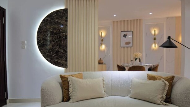 A modern living room with a round marble accent wall, a sofa with patterned cushions, and a dining area with a table and chairs. - Luxurious 1-bedroom apartment & 1 African-style bedroom (Dakar)