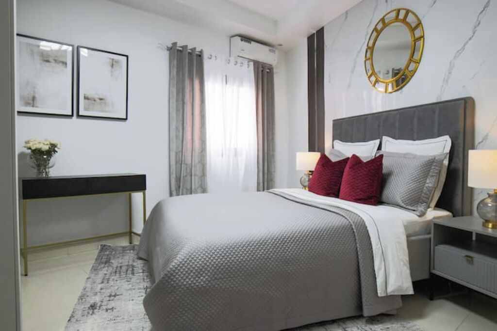 A modern bedroom with a bed, bedside tables, a desk, and a mirror.