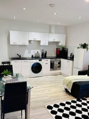 A modern kitchen with white cabinets, a washing machine, and a dining area with a glass table and chairs.