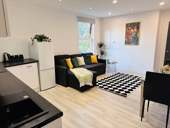A modern kitchen with a black countertop and white cabinets, a black sofa with yellow cushions, a black and white rug, and a painting of a cheetah on the wall.