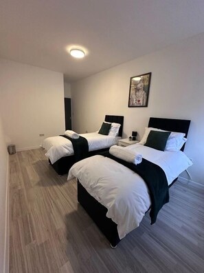 A hotel room with two beds, a small bedside table, a wall-mounted picture, and a light ceiling fixture.